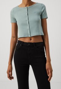 T-shirt côtelé bleu clair raccourci à manches courtes, fermeture par boutons et logo brodé. Associé à un jean noir taille haute.