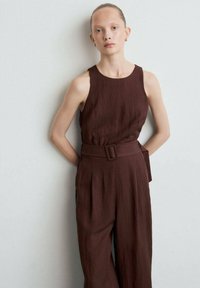 Bruine linnen jumpsuit met een mouwloze pasvorm, een ceintuur in de taille, een losse fit en een subtiele textuur. Eenvoudige en functionele tailoring.
