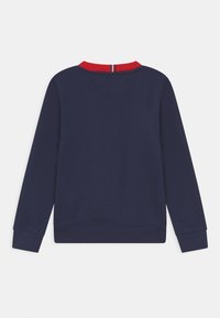 Marineblauwe trui met een rood geribbeld boordje en V-hals. Voorzien van lange mouwen en geribbelde manchetten, gemaakt van een glad en zacht materiaal.