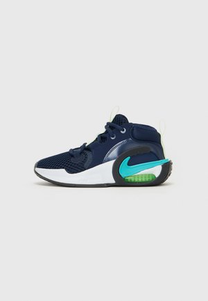 Zapatilla deportiva azul marino con parte superior de malla, acentos verdes y suela de goma negra. Cuenta con punta redondeada y cordones con una lengüeta en el talón.