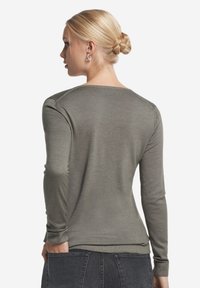 Olivgrön långärmad tröja i mjukt material, med rundad halsringning och ribbade ärmslut, buren tillsammans med mörka denimbyxor.