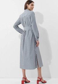 Gestreiftes langärmliges Kleid in Blau und Weiß mit cinch-tailliertem Bund, seitlichen Schlitzern und einem Kragen. Kombiniert mit roten Blockabsatzsandalen.