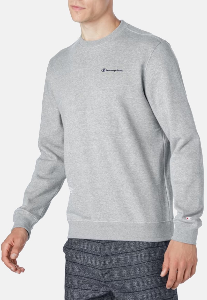 Sudadera gris con cuello redondo, puños y dobladillo acanalados. Presenta un pequeño logo bordado de "Champion" en azul oscuro en el pecho.