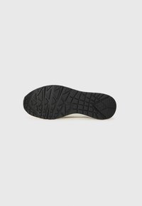 Semelle de chaussure en caoutchouc noir avec des motifs de bande de roulement texturés, présentant de profonds sillons et des sections surélevées pour une meilleure adhérence.