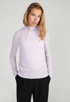 Helllila Rollkragenpullover aus weichem Strickmaterial, mit langen Ärmeln und passender Silhouette, kombiniert mit schwarzen Hosen.
