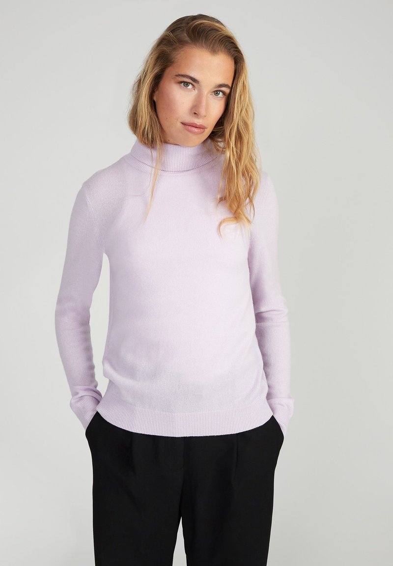 Maglione a collo alto di un delicato colore lilla in un morbido tessuto a maglia, con maniche lunghe e una silhouette aderente, abbinato a pantaloni neri.