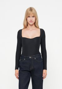 Bodysuit noir à manches longues avec un décolleté carré, en tissu lisse et à design ajusté, associé à un jean en denim foncé taille haute.