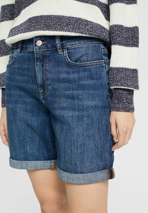 Mittellange hochgekrempelte blaue Jeansshorts, getragen mit einem marineblau-weiß gestreiften Strickpullover an einer Person.