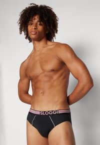 Schwarze Shorts mit einem mehrfarbigen elastischen Bund, der den Markennamen "SLOGGI" trägt. Glatter Stoff mit Kontrastnähten.