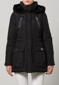 Cappotto imbottito nero con cappuccio foderato in pelliccia sintetica, due tasche frontali con zip e tasche sul petto con zip. Presenta una silhouette aderente e dettagli con toggle.