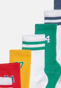 Cinque paia di calze da crew in rosso, giallo, verde, bianco e blu navy. Ognuna presenta una texture a coste con strisce a contrasto e numeri stampati sui lati.