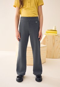 Tumedat halli värvi spordipüksid, millel on laiad sääred ja sile tekstuur. Varustatud elastse vöökohaga ning väikese logoga. Kombineeritud kollase polosärgiga.