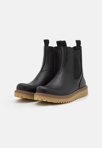 Bottines Chelsea en cuir noir avec panneaux élastiques sur les côtés, bout arrondi et semelle en caoutchouc marron texturé. Équipées de tirettes pour un enfilage facile.