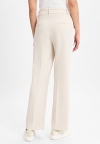 Beige wijde broek met een gladde textuur, voorzien van twee achterzakken en een hoge taille. Gepaard met off-white sneakers.
