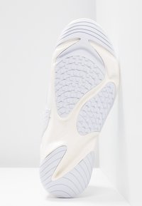 Semelle blanche de sneaker avec des motifs de grip texturés incluant des plots carrés et des lignes courbes, conçue pour la traction et le soutien.