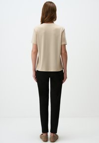 Beige kortekorte mouw top met een ronde hals, gecombineerd met strak zwarte broek. Zacht materiaal met een gladde textuur. Eenvoudig ontwerp.