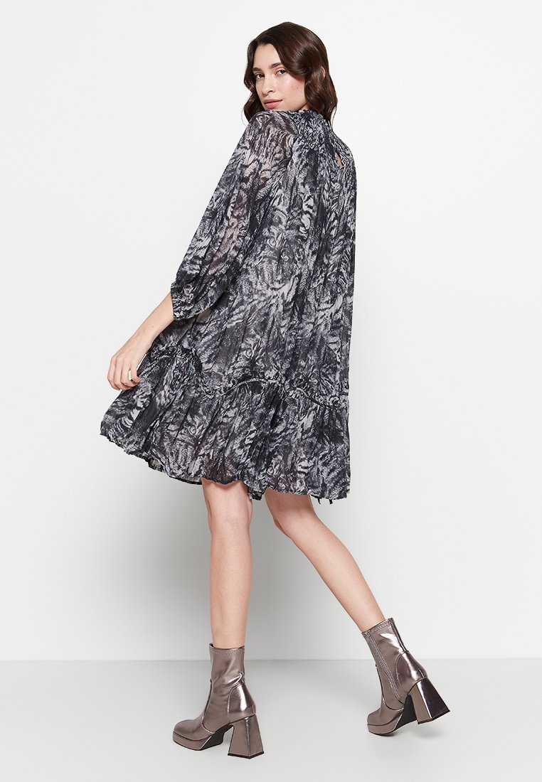 Korte mouwen, knielange jurk in zwart en grijs bloemenpatroon met een rucheszoom. Gemaakt met metallic grijze enkelhoge laarzen.