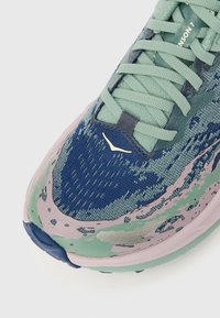 Ελαφρύ αθλητικό παπούτσι τρεξίματος με υφασμένο επάνω μέρος σε αποχρώσ εις πράσινου και μπλε, ρόζ και γκρι λεπτομέρειες, με περιγραμμωμένη σόλα και επενδυμένη γλώσσα.