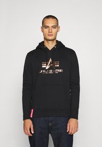 Felpa nera con cappuccio e lacci, tasca frontale e stampa del logo metallica. Materiale morbido con polsini e orlo a coste. Sfondo bianco.