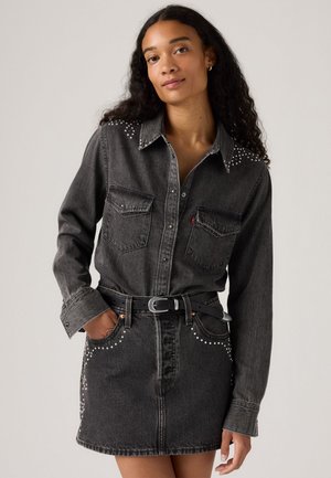 Zwarte denim overhemd met zilveren studs op de schouders, gecombineerd met een bijpassende rok met studdetails en een zwarte riem.