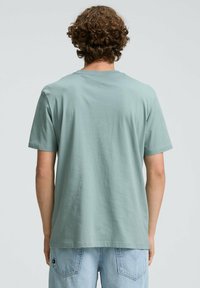 Jasnozielona bawełniana koszulka z luźnym krojem, krótkimi rękawami i okrągłym dekoltem. Gładka tekstura bez widocznych wzorów czy akcentów.