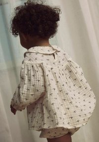 Lengvai tekstūruotas medvilnės marškinėliai su suapvalintu apykakle, pasižymintys mažo mygtuko uždarymu ir tamsių spalvų mažų palmės medelių raštu.