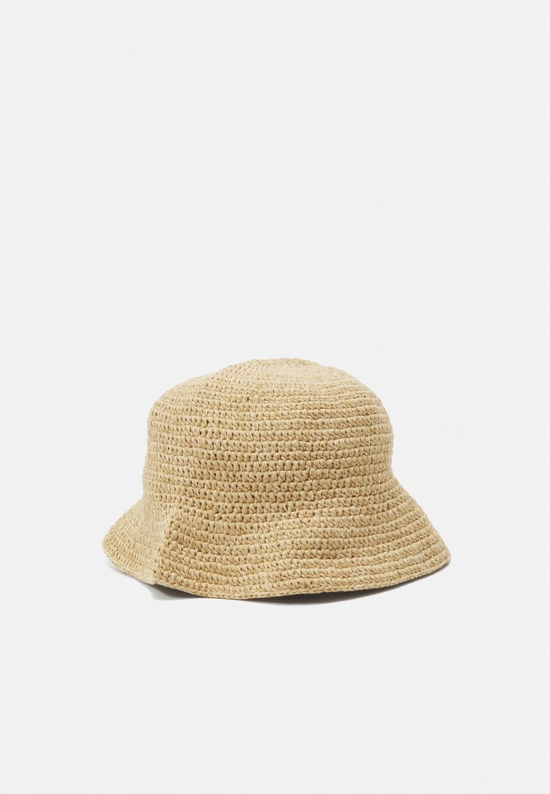 Chapeau bob tissé beige avec une structure simple et douce et un bord court incliné vers le bas sur un fond uni clair.