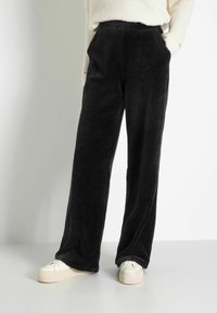 Pantalons en velours côtelé noir à jambes larges avec texture à côtes verticales, dotés de poches avant et d'une taille haute, associés à des baskets à plateforme crème.