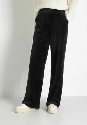 Pantalons en velours côtelé noir à jambes larges avec texture à côtes verticales, dotés de poches avant et d'une taille haute, associés à des baskets à plateforme crème.