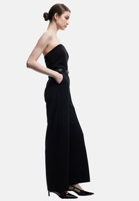 Czarny kombinezon bez ramiączek z dopasowaną górą, szerokimi nogawkami i bocznymi kieszeniami. W połączeniu z czarnymi szpilkami i wąskim czarnym paskiem.