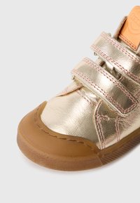 Złote metaliczne sneakersy z trzema rzepami, różowym przeszyciem i podeszwa gumową. Okrągły czubek z teksturowaną powierzchnią.