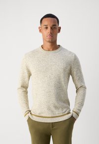 Lys beige strikket genser med rund hals, med et teksturert, spraglete mønster. Ribbestrikkede mansjetter og sømkant med en kontrasterende stripe.