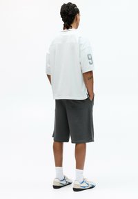 White oversized t-shirt with gray accents and number 9, paired with gray shorts. Shoes are beige with blue details, white socks visible.