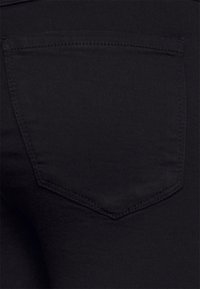 Černá denimová látka s jedním zadním kapsou, která má jemný šitý vzor. Materiál má hladkou texturu s mírným leskem.