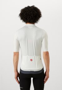 Maillot de cyclisme léger à manches courtes en blanc avec une finition texturée, comportant des poches arrière et un petit logo.
