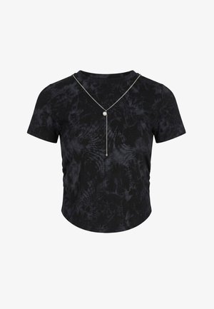 Czarny, barwiony metodą tie-dye t-shirt z krótkim rękawem oraz srebrny naszyjnik w kształcie litery Y z małą perłą i pionową zawieszką z łańcuszka.