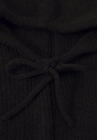 Black knitted fabric tied in a bow, showing textured yarn and soft material close-up.
