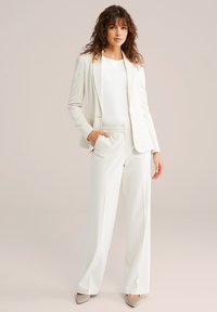 Biely prispôsobený blejzer a zodpovedajúce nohavice z hladkej látky. Svetlý, neutrálna farba s klasickým strihom a jemným leskom. Jednoduchý, elegantný dizajn.