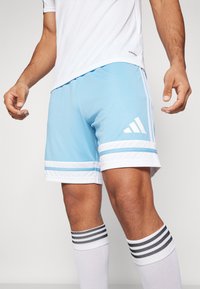 Világoskék sportnadrág fehér vízszintes csíkokkal és három fehér adidas csíkkal; nedvességelvezető anyaggal és puha textúrával rendelkezik.