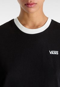 Camiseta negra de manga corta con un cuello acanalado blanco, que presenta el logo blanco de "VANS" en la parte izquierda del pecho. Tela de algodón suave.