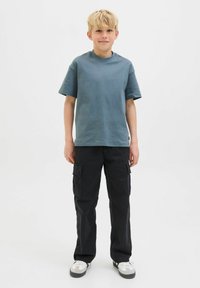 Maglietta grigia a maniche corte, abbinata a pantaloni cargo neri con ampie tasche laterali, e sneakers bianche. Design semplice e casual.