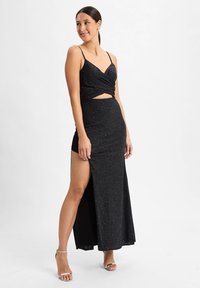 Zwarte, sprankelende avondjurk met dunne bandjes, een gedraaide corsage, een uitgesneden taille en een zijsplit. Glad textuur, vloerlange ontwerp.