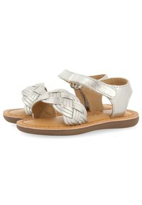 Sandali in pelle intrecciata argentata con punta aperta, cinturino regolabile e suola marrone. Struttura liscia con design piatto, adatti per un uso casual.