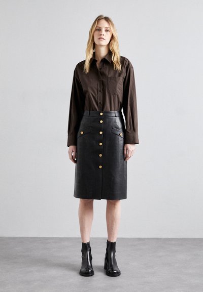 Zwarte leren midirok met knopen aan de voorkant en opgestikte zakken, met een reliëfpatroon en gouden hardware. Gecombineerd met een bruine blouse met knopen.