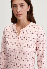 Maglietta a maniche lunghe rosa con un motivo floreale ripetuto in una tonalità più scura, dotata di un collo henley con bottoni e una texture di tessuto morbido.
