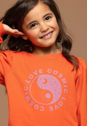 Oranje sweatshirt met lange mouwen heeft een cirkelvormige grafiek in lila, die kosmische motieven zoals sterren en een halve maan afbeeldt.
