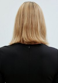 Schwarzes Kleid mit einem strukturierten Design, das einen Reißverschluss auf der Rückseite hat. Helles braunes, glattes Haar ist über dem Ausschnitt sichtbar.