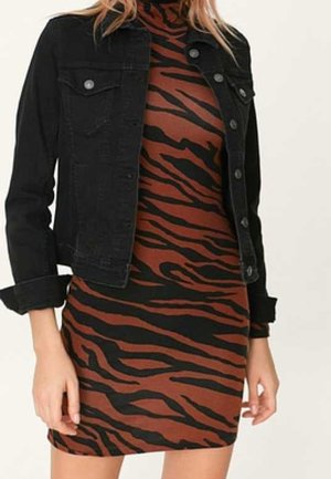 Femme portant une robe ajustée rayée tigre marron et noire, associée à une veste en jean noire courte avec les manches retroussées.