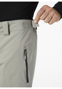 Grijze broeken met een gladde textuur, voorzien van een klittenband verstelriem bij de taille en een ritszak aan de zijkant met een zwarte rits.