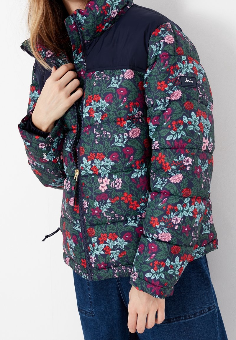 Vadderad jacka med ett blommönster i gröna, röda och rosa nyanser. Marinblå övre del, dragkedja fram och elastiska ärmslut.